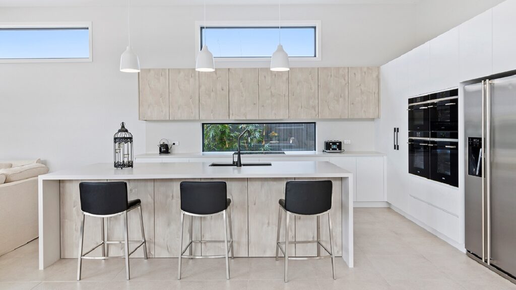Modern coastal kitchen benchtop ideas featuring white stone benchtops with light timber cabinetry, black bar stools, and contemporary pendant lighting in an Australian home