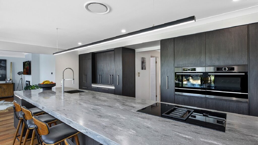 Modern industrial kitchen featuring dark cabinetry, sleek black appliances, and a stone island bench — a perfect example of industrial kitchen decor ideas.