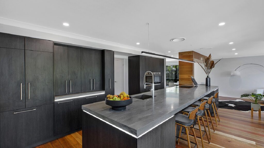 Sleek modern industrial kitchen inspiration featuring dark timber cabinetry, stone benchtops, integrated appliances, and a spacious island with contemporary seating.