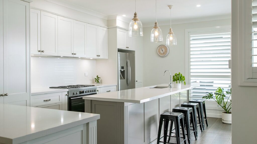 Bright Hampton style kitchen with white shaker cabinets, stone island benchtop, pendant lighting, and coastal-inspired design creating a light-filled, elegant space.